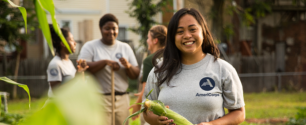 Decorative image. An AmeriCorps member holds an ear of corn.